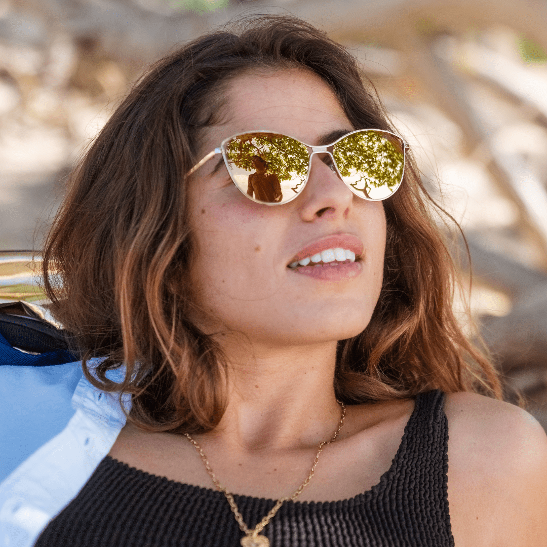 Woman wearing gold reflective sunglasses with a blurred natural background