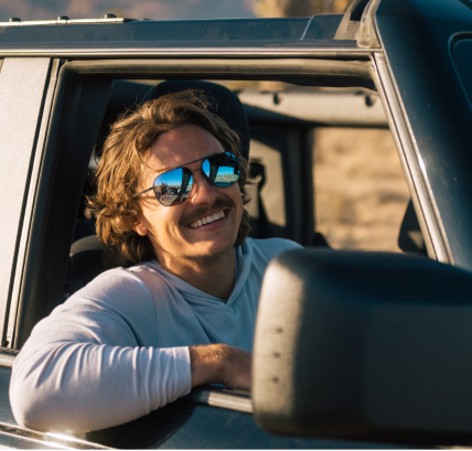 Man with sunglasses smiling from a car in a desert setting